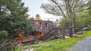 A building with a wooden staircase leading to a deck, surrounded by greenery and a gravel path. - Walk to Slopes! Beech Mountain Condo, Pet Friendly (Banner Elk)