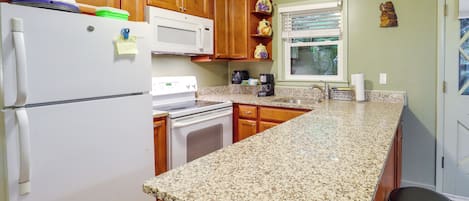 A kitchen with wooden cabinets, a white refrigerator, a microwave, a stove, and a granite countertop.