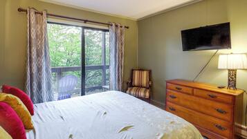 A bedroom with a bed, a dresser, a chair, a television, and a window with curtains.