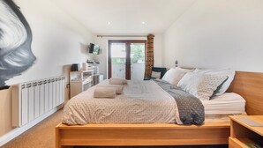 Un dormitorio con cama, mesitas de noche, un radiador, televisor y un balcón con cortina.