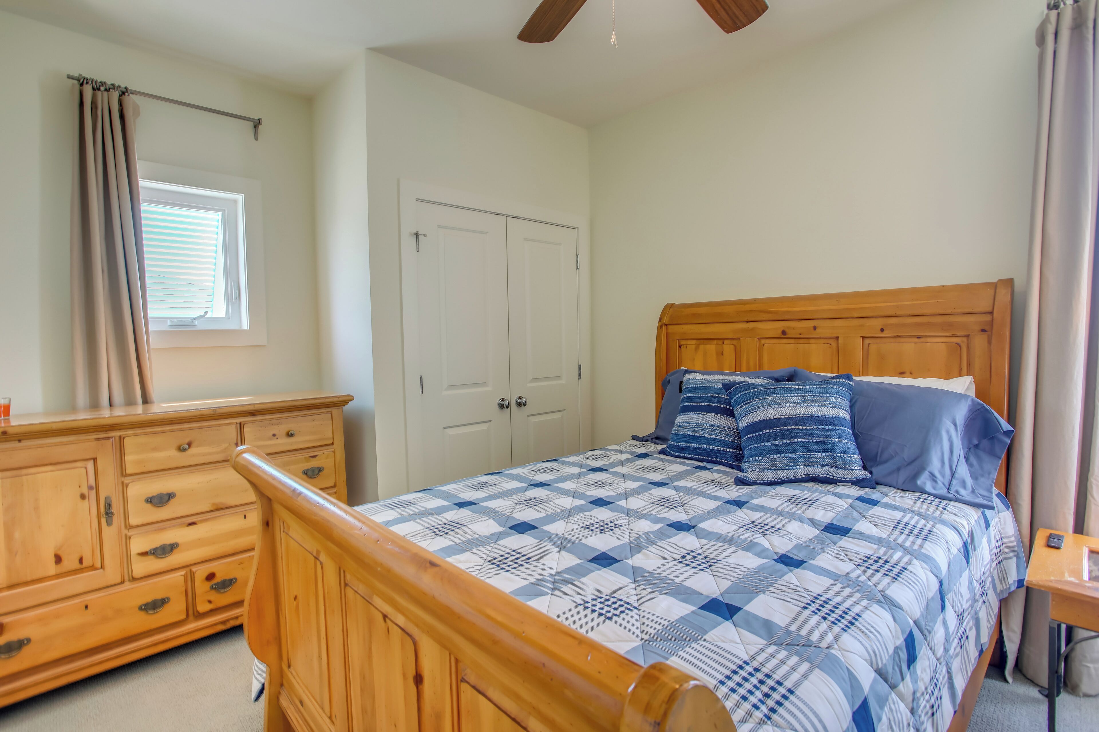 A bedroom with a wooden bed, a dresser, a window with blinds, and a ceiling fan.