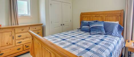 A bedroom with a wooden bed, a dresser, a window with blinds, and a ceiling fan.