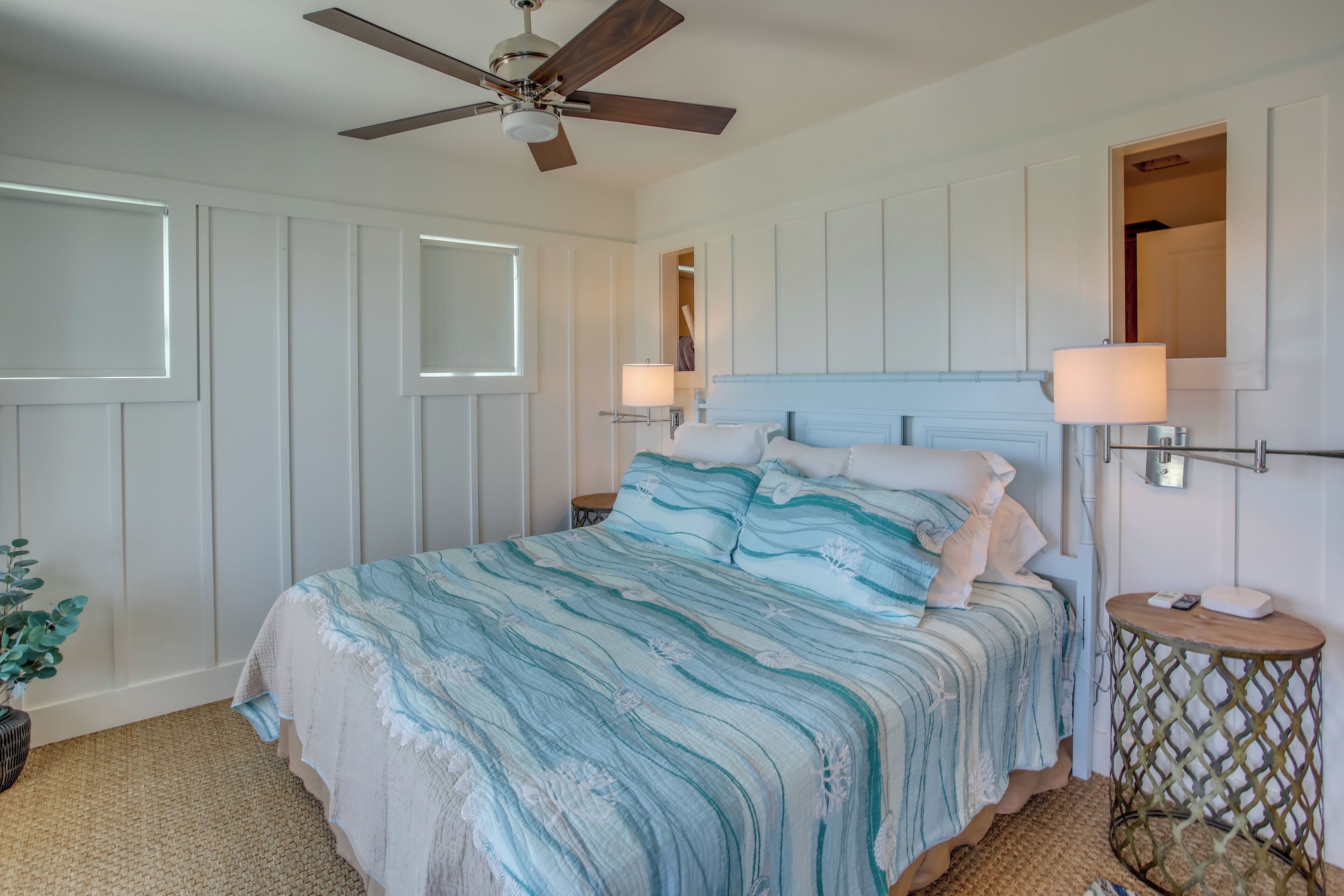 A bedroom with a bed, ceiling fan, bedside lamps, and a small round table.