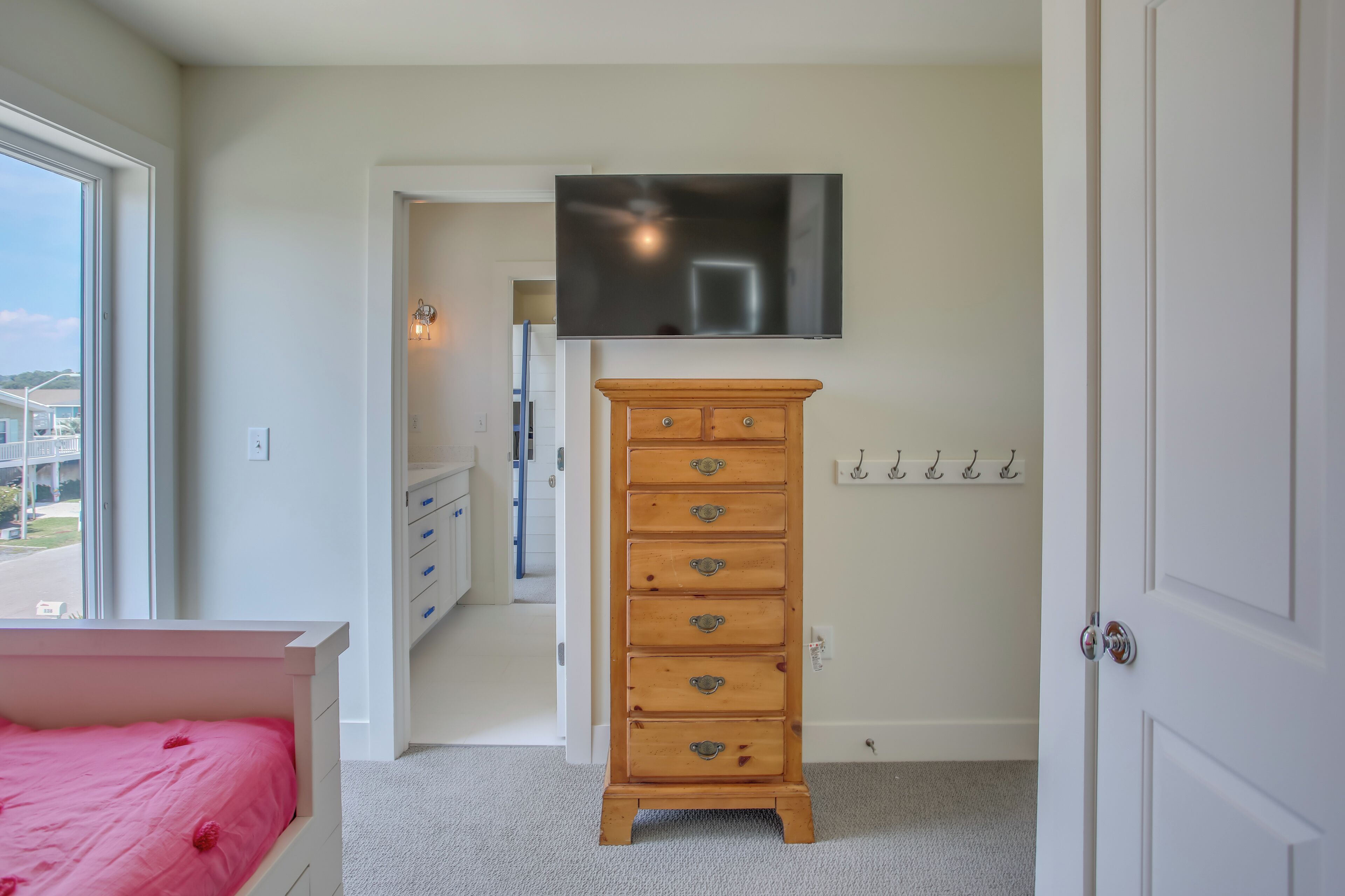 A bedroom with a bed, a dresser, a TV mounted on the wall, and a door.