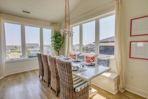 Comedor con sillas de mimbre, una mesa blanca y vistas del barrio a través de amplios ventanales.