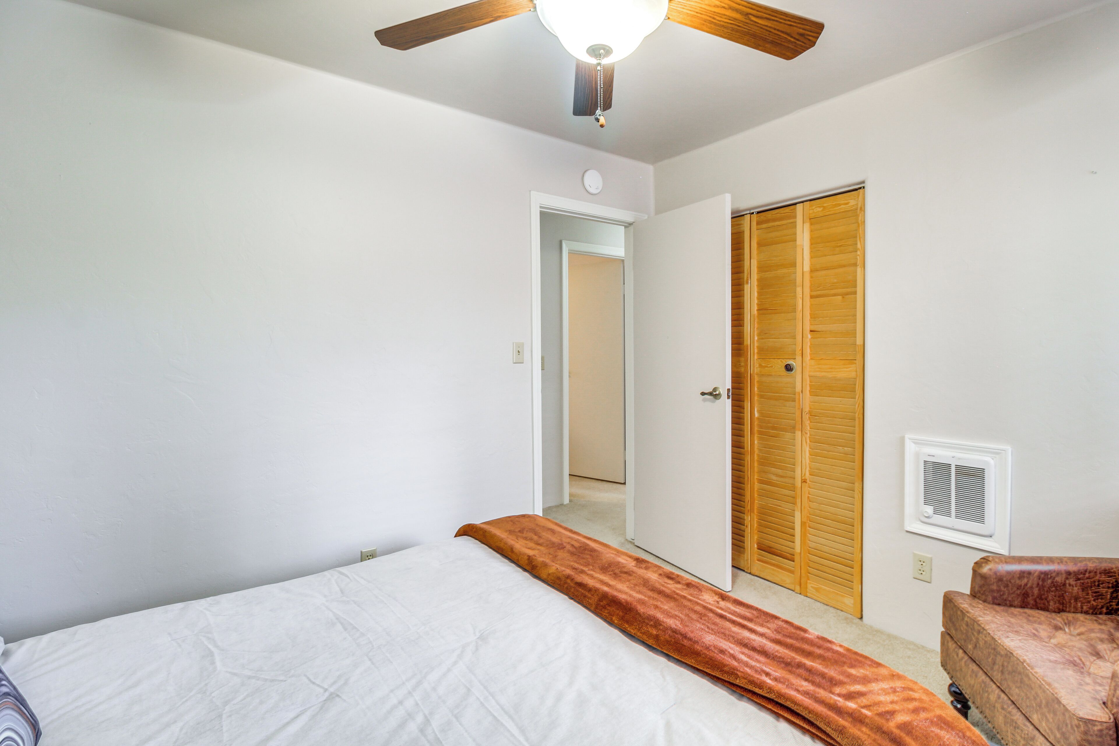 A bedroom with a bed, a ceiling fan, a wooden closet, and a wall-mounted air conditioning unit.