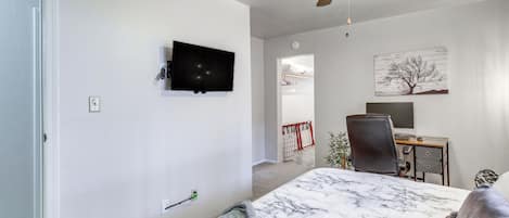 Een slaapkamer met een bed, een bureau, een stoel, een plafondventilator, een televisie en een schilderij aan de muur.