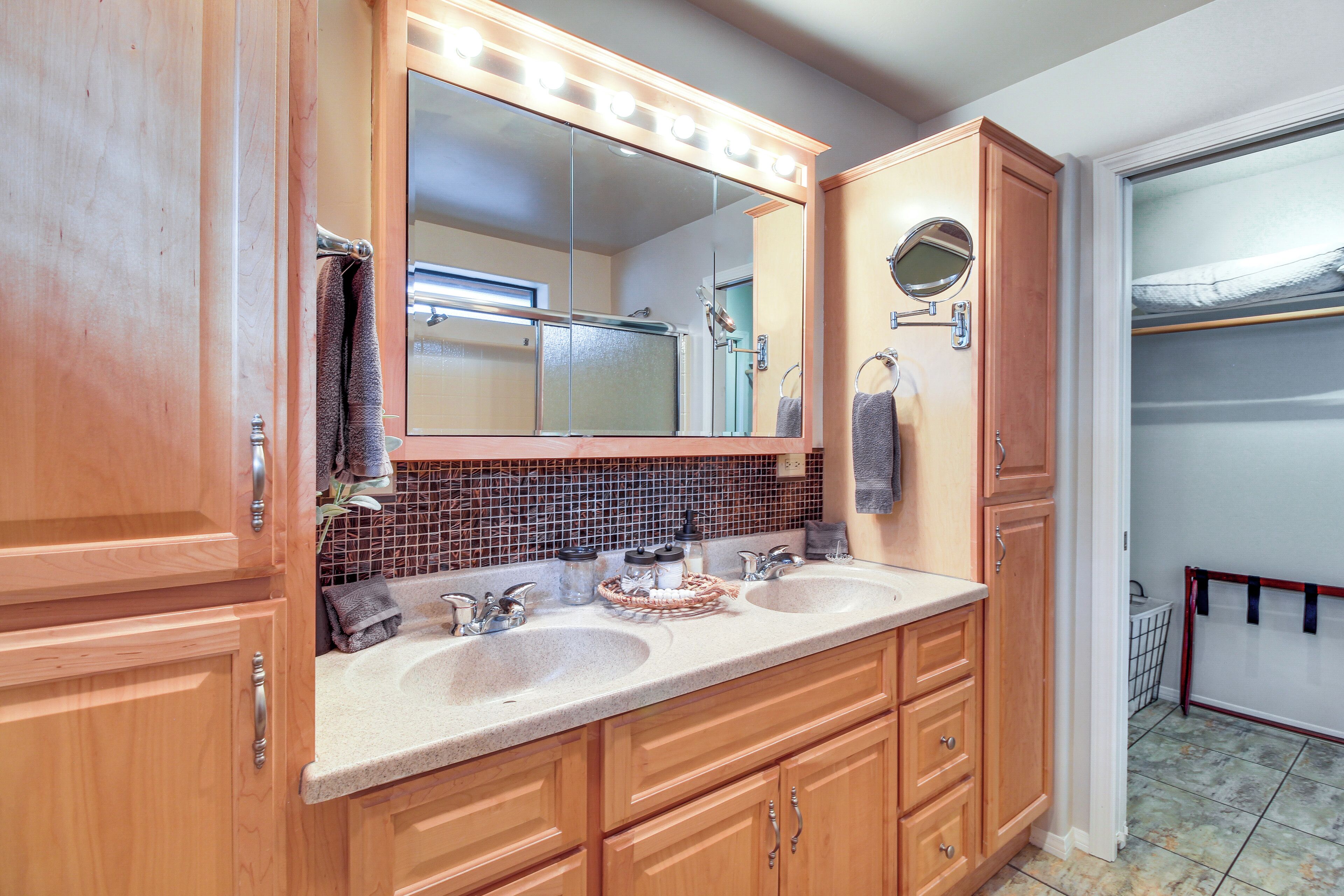 A bathroom with wooden cabinets, a double sink vanity, a mirror with lights, and a towel rack.