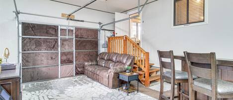 A spacious room with a ceiling fan, a brown leather sofa, a wooden chair, and a patterned rug.