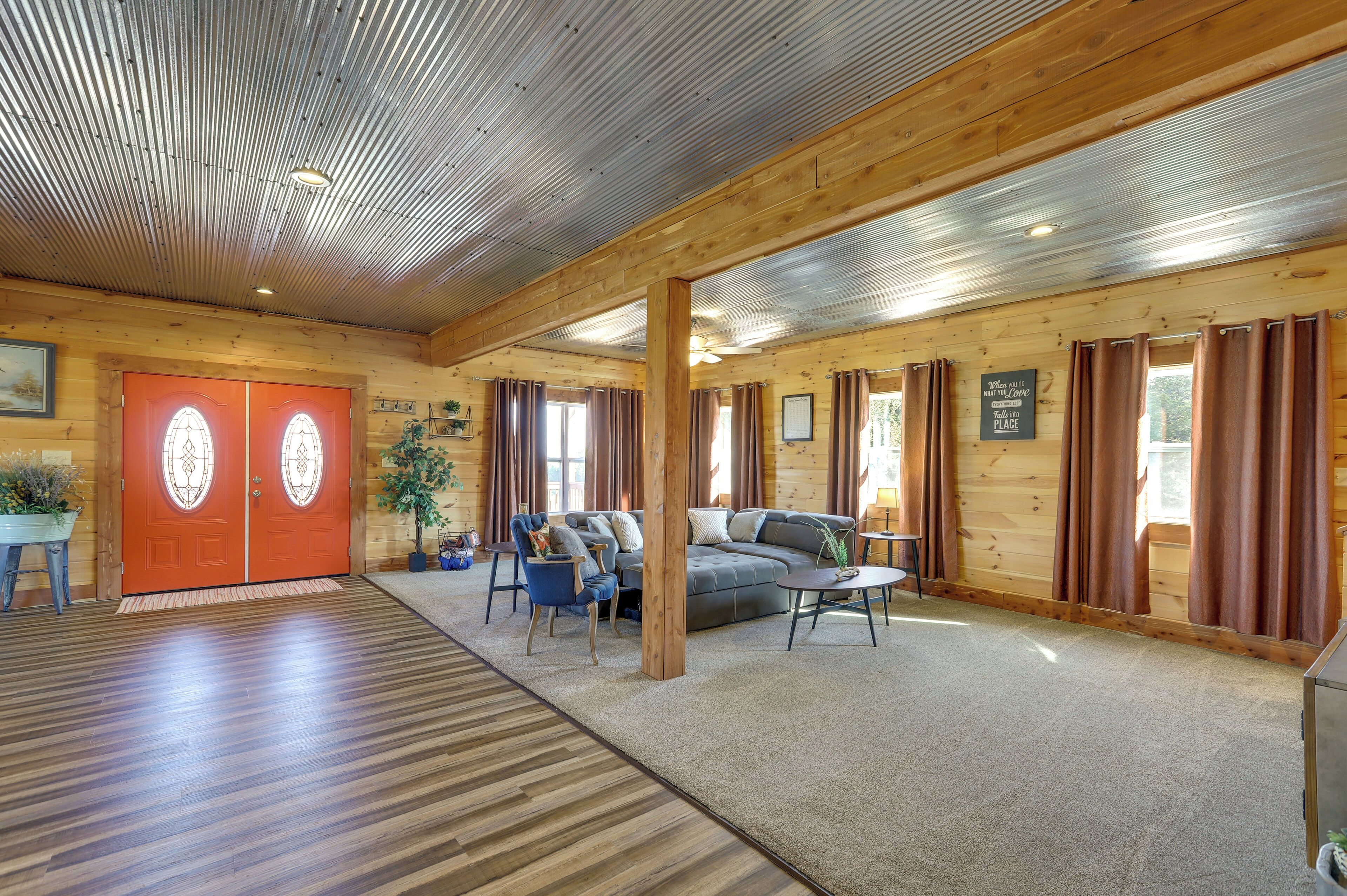 A spacious room with a wooden floor, a red door with glass panels, a grey sofa, blue chairs, and a small table.