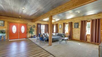 A spacious room with a wooden floor, a red door with glass panels, a grey sofa, blue chairs, and a small table.