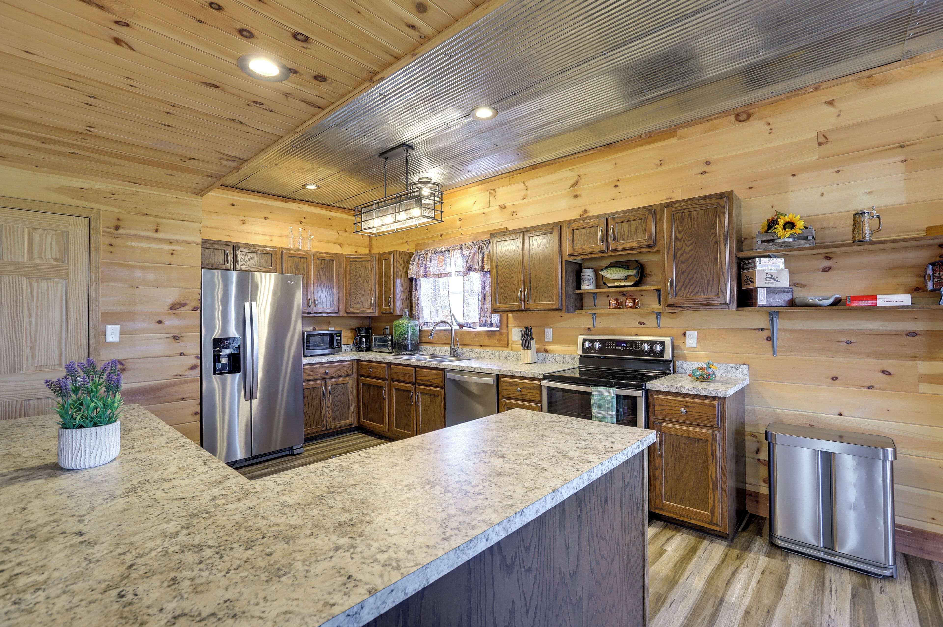 A kitchen with wooden walls, granite countertops, stainless steel appliances, and a trash can.