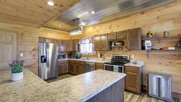 A kitchen with wooden walls, granite countertops, stainless steel appliances, and a trash can.
