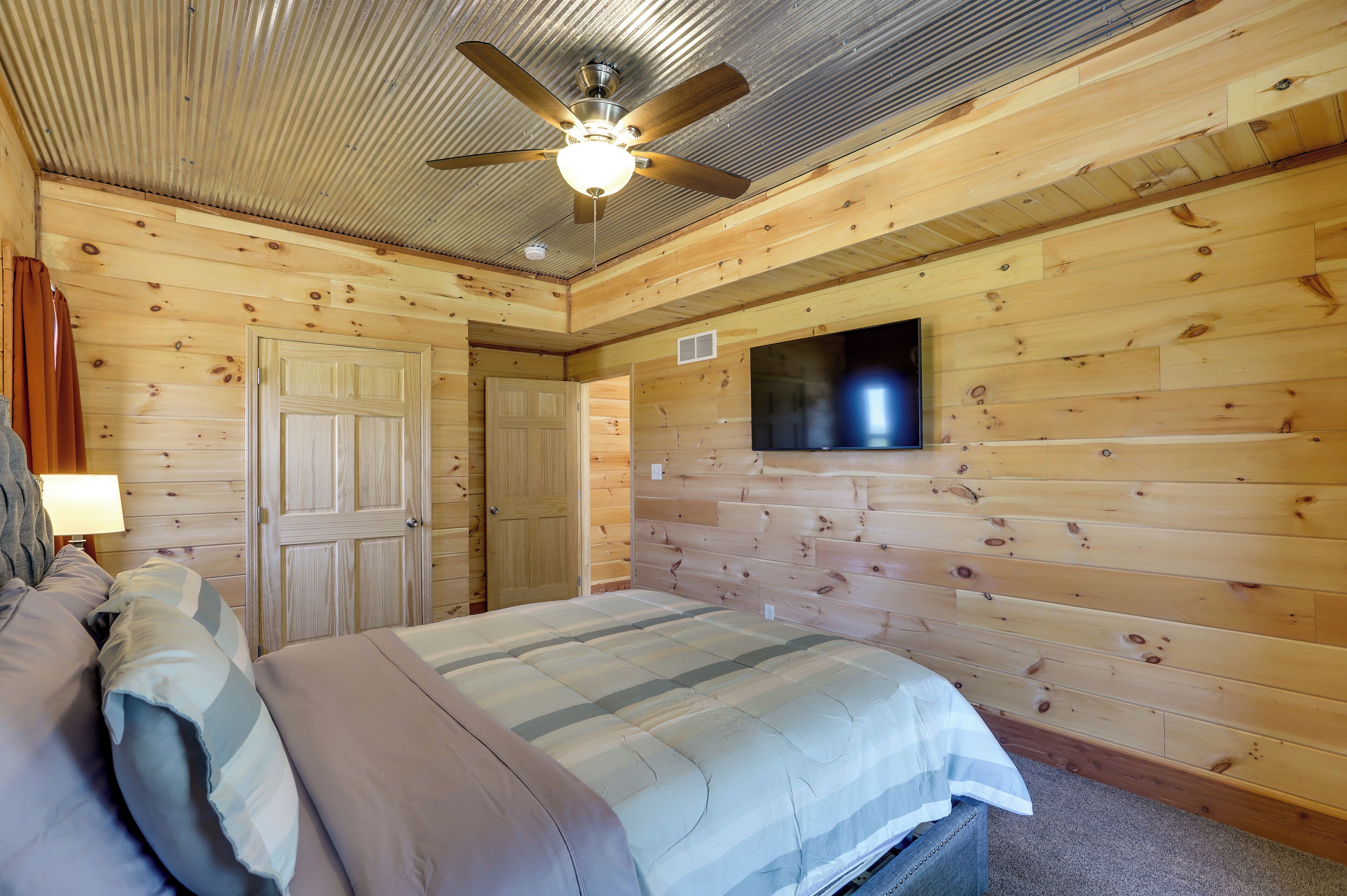 A wooden-paneled bedroom with a bed, a ceiling fan, and a mounted TV.