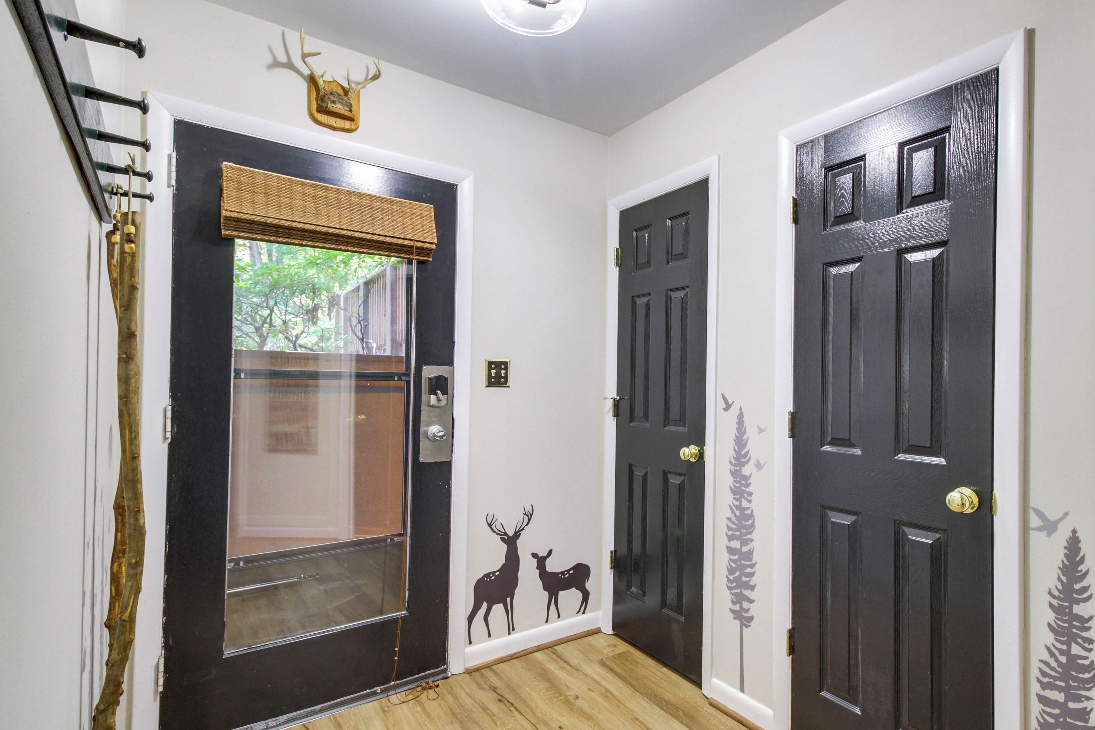 A hallway with a black door, a glass door, and a wall decal of deer.