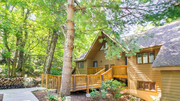 A cabin with a wooden deck, surrounded by trees and a stone wall. - Wintergreen Resort Condo w/ Deck, 0.3 Mi to Slopes (Nellysford)