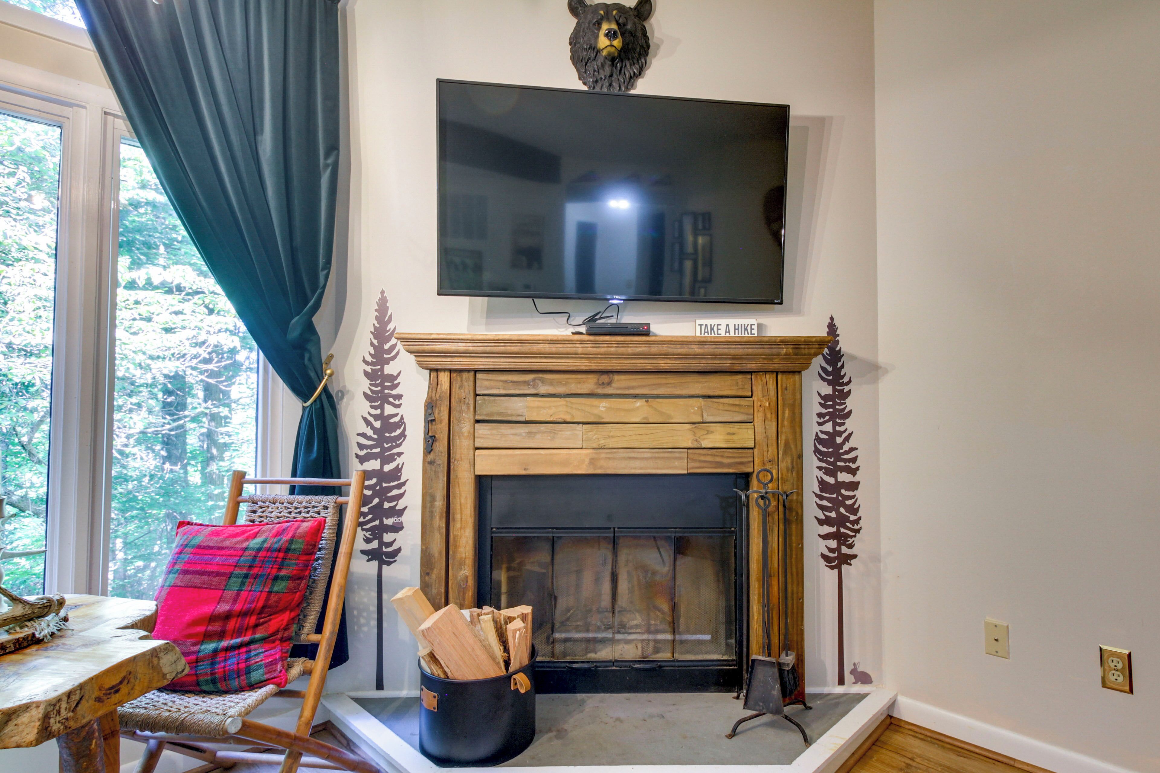 Una sala de estar con chimenea, un televisor montado encima y un sillón acogedor con un cojín escocés.