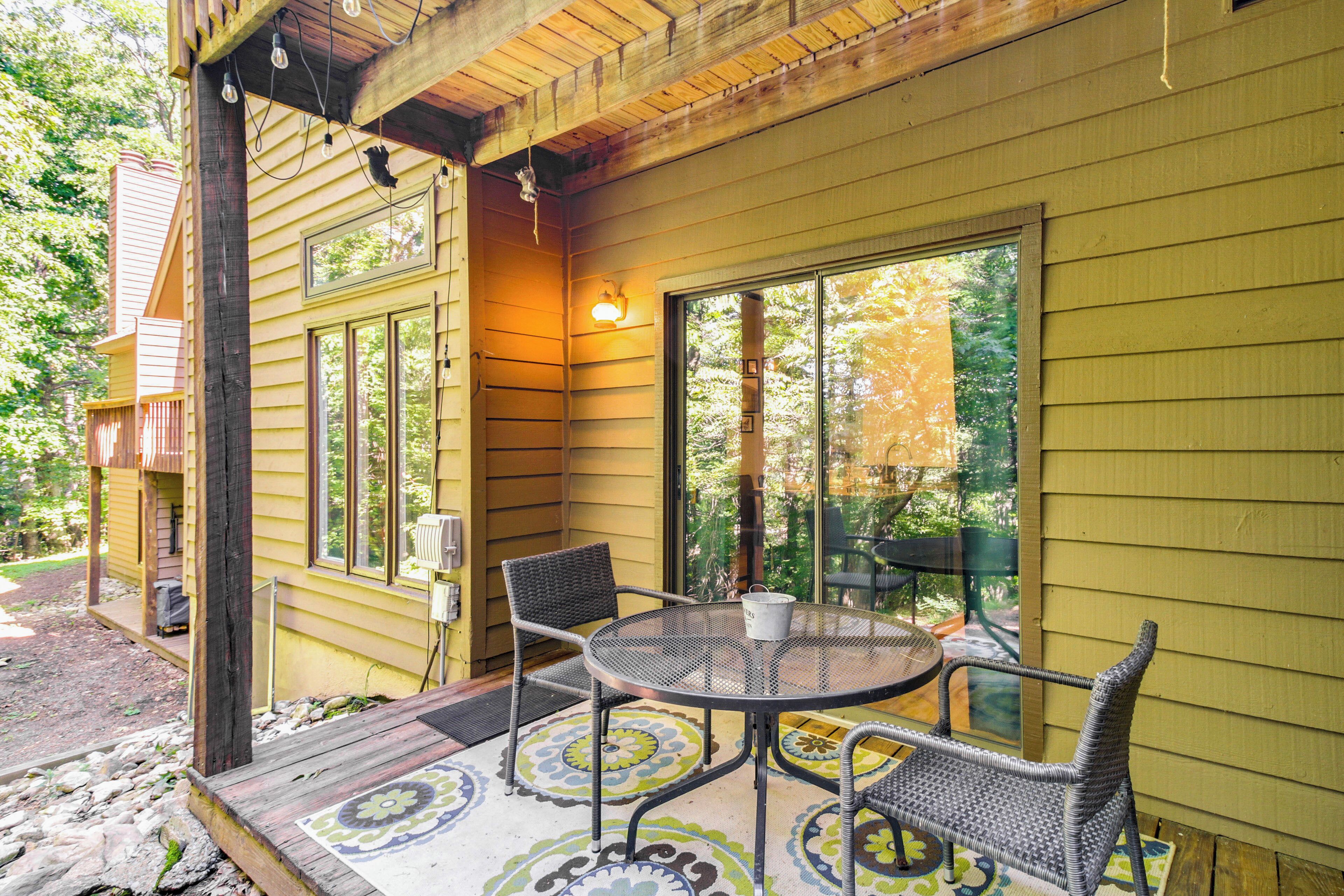 Une maison en bois dotée d’un porche comprenant une table ronde et des chaises en osier, de grandes fenêtres et un luminaire.