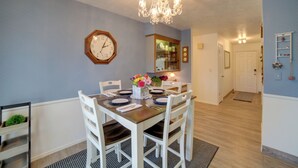 A dining area with a wooden table set for four, white chairs, a chandelier, a clock, and a mirror on the wall. - Simple + Charming Idaho Retreat w/ Patio! (Idaho Falls)
