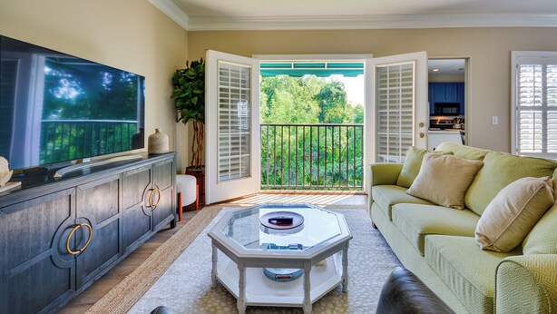 A living room with a glass coffee table, a sofa, and a television on a cabinet. - Greensboro Condo Rental Near Hospital & Trails! (Greensboro)