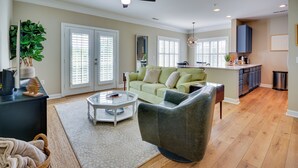 A spacious living room with a green sofa, a glass coffee table, and a dark armchair. - Greensboro Condo Rental Near Hospital & Trails! (Greensboro)