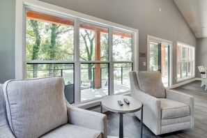 A spacious room with large windows, two armchairs, a small round table, and a remote control on the table. - Modern Norfork River Cabin Rental w/ Shared Dock! (Mountain Home)