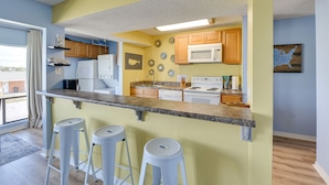 A kitchen with a bar area, wooden cabinets, a microwave, and a stove. - Bright Destin Condo w/ Community Pool! (Destin)