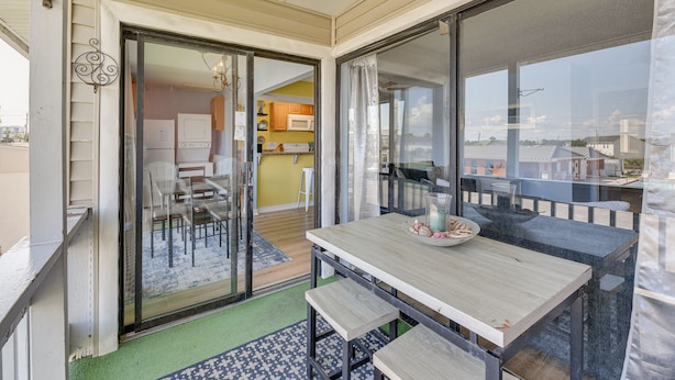 A balcony with a table and chairs, a sliding glass door leading to a kitchen, and a view of the surrounding area. - Bright Destin Condo w/ Community Pool! (Destin)