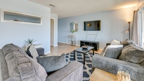 A modern living room with grey sofas, a coffee table, a TV mounted on the wall, and a small side table with a plant. - Bright Destin Condo w/ Community Pool! (Destin)