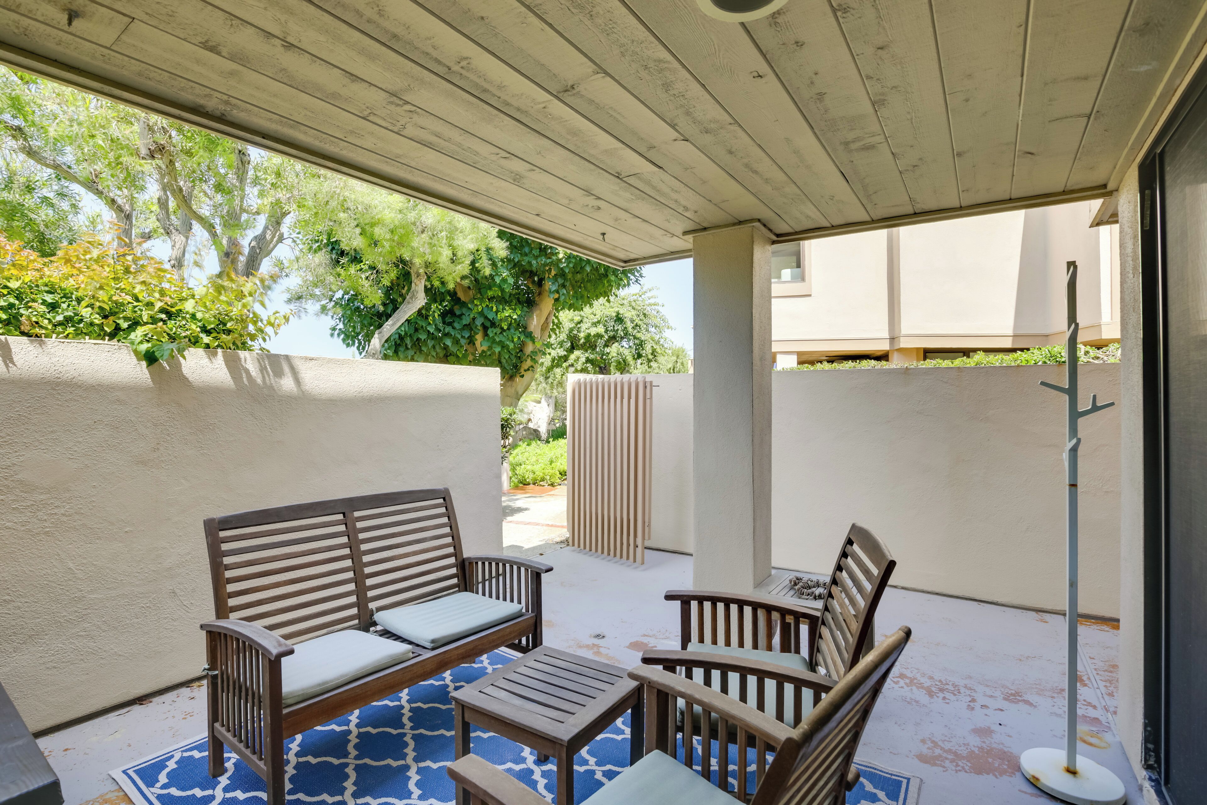 An outdoor patio with wooden furniture, including a sofa and chairs, and a small table.