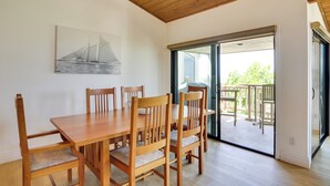 Un comedor con una mesa y sillas de madera, un cuadro de veleros y un ventanal corredizo que da a un patio exterior.