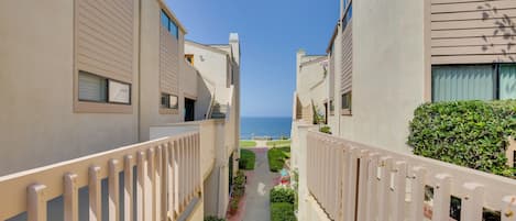 A narrow pathway between buildings with a view of the ocean.