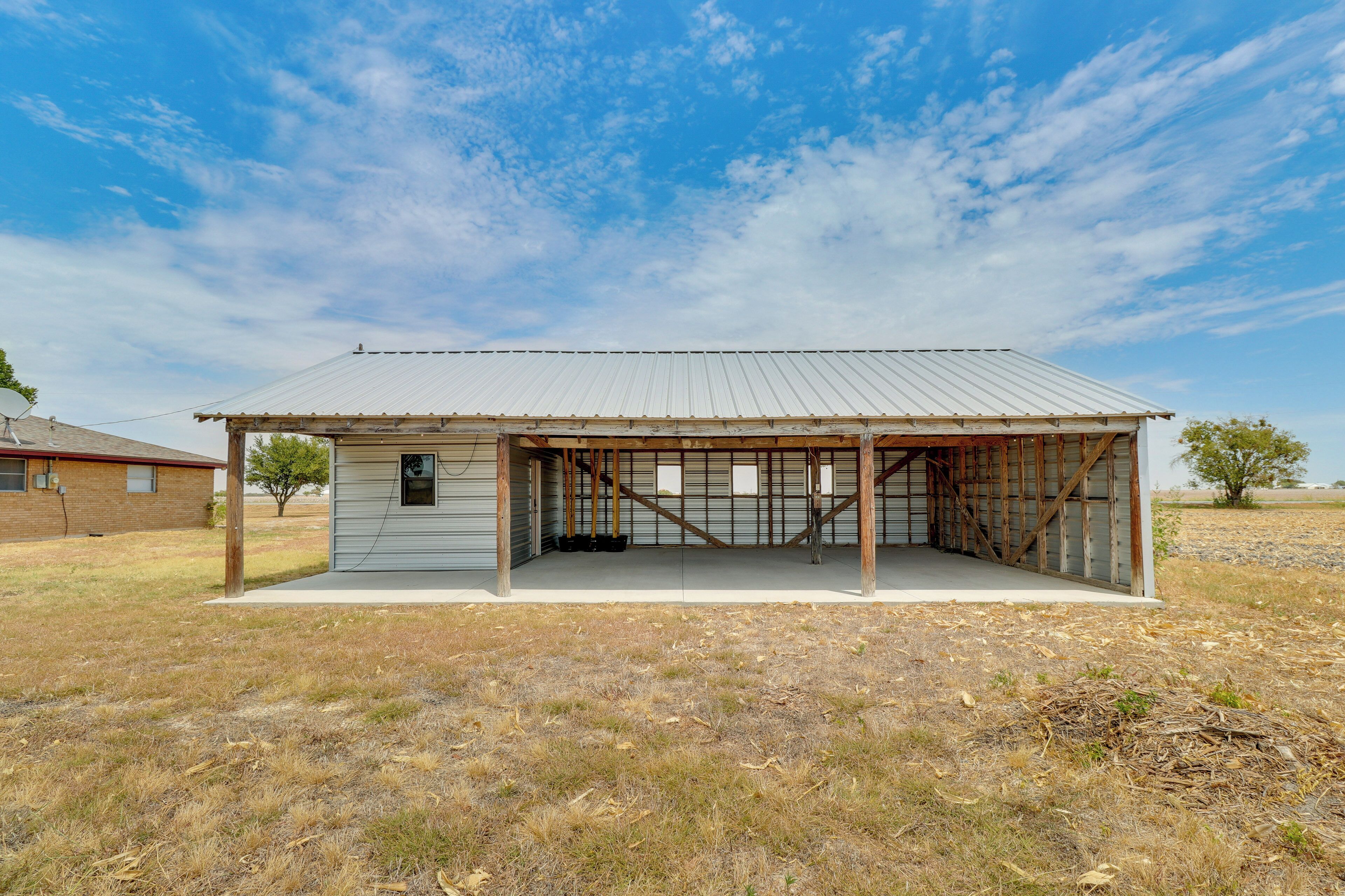 A single-story building with a metal roof and wooden framework, surrounded by dry grass and a clear sky.