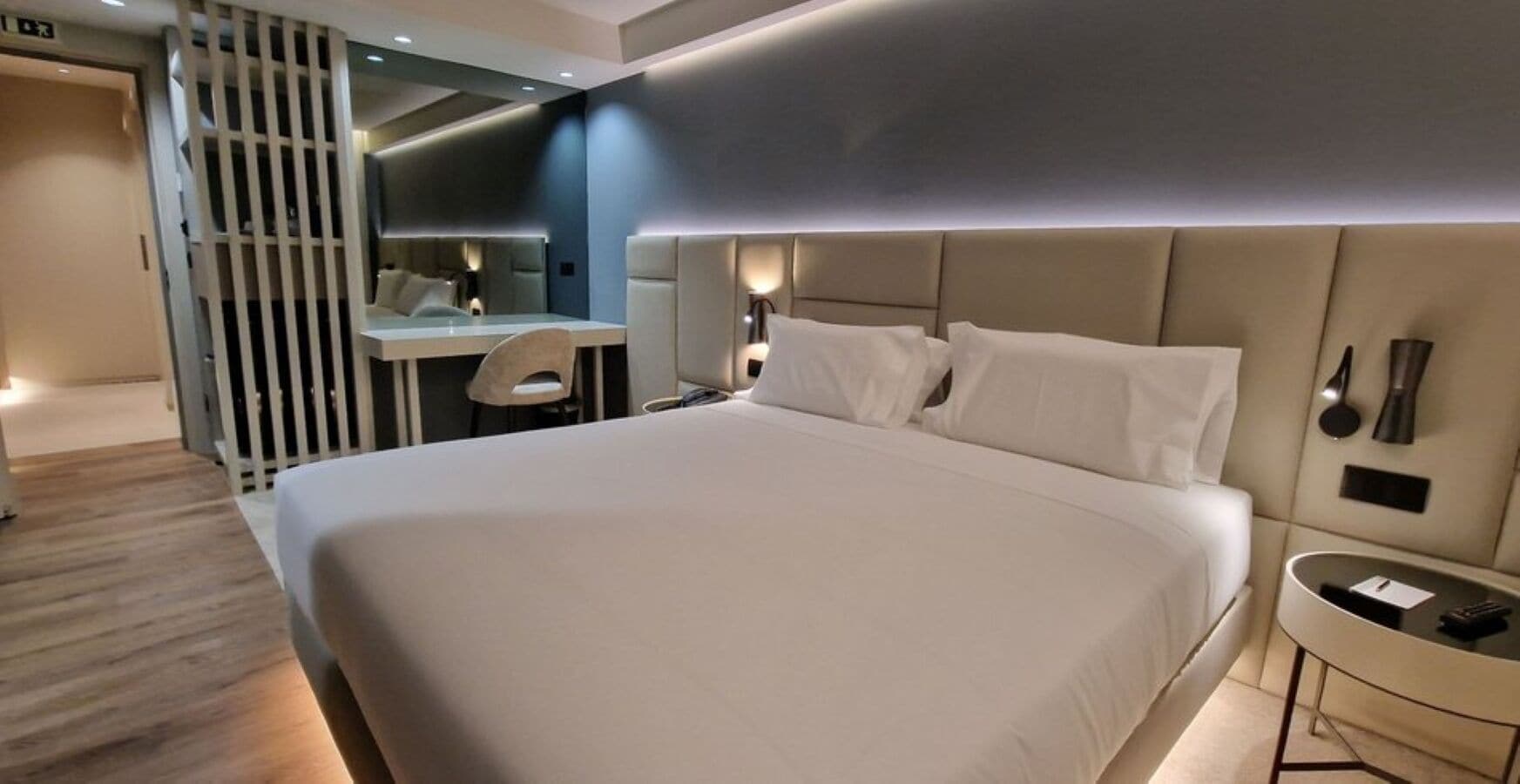 A modern hotel room with a large bed, a desk, and a chair.