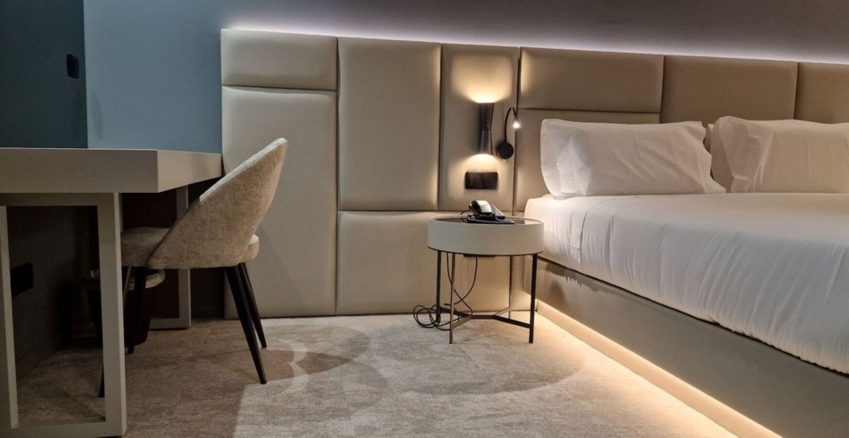 A modern bedroom with a bed, bedside table, chair, and wall-mounted light.