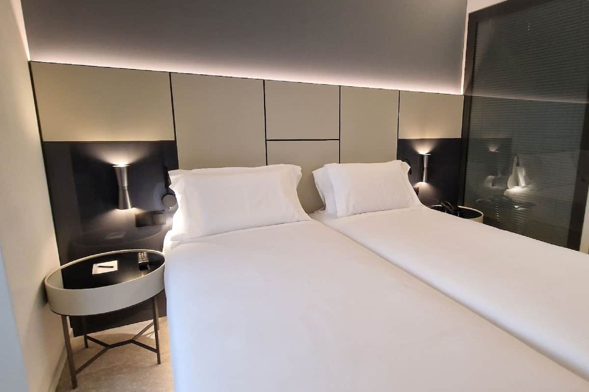 Una habitación de hotel moderna con una cama grande, mesitas de noche y un separador de vidrio.