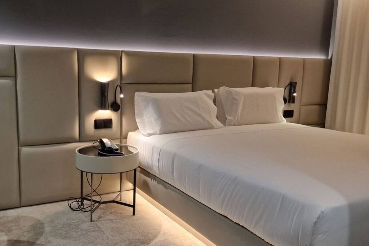 Una habitación de hotel moderna con una cama grande, una mesita de noche con teléfono y una silla.