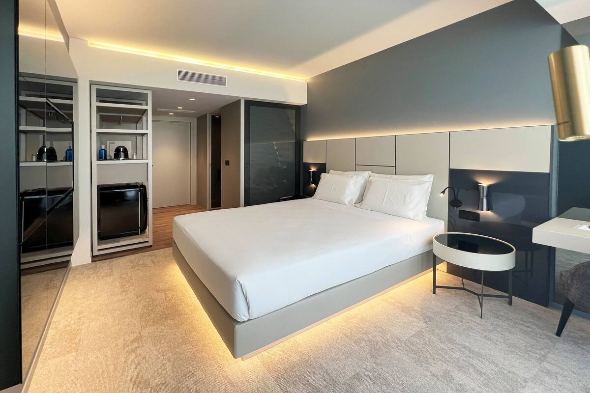 Una habitación de hotel moderna con una cama grande, un armario empotrado, un escritorio pequeño y una zona de estar.