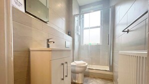 Une salle de bain moderne équipée de toilettes, d’une douche et d’une fenêtre laissant entrer la lumière naturelle.