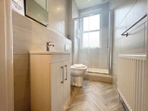 A modern bathroom with a toilet, shower, and a window providing natural light. - 2-Bed Victorian Elegance (Cheshire West and Chester)