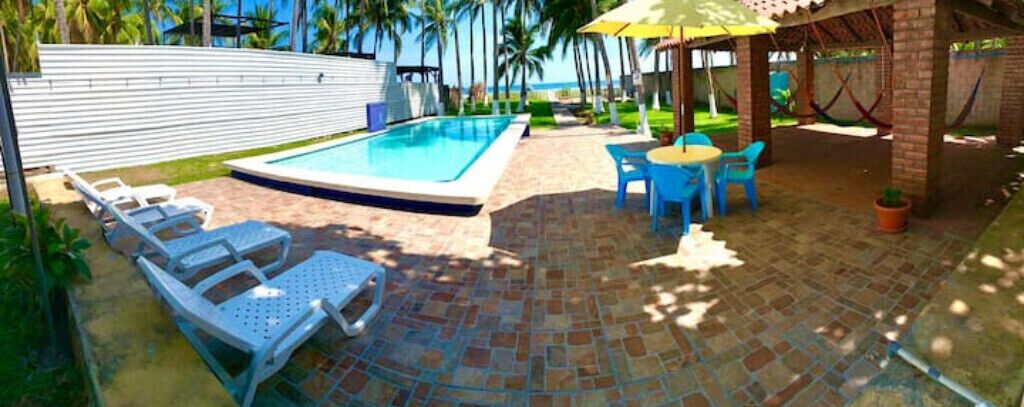A pool area with lounge chairs, a table, and a covered seating area.