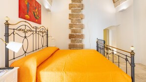 A bedroom with a bed, a nightstand, a lamp, a painting, and a stone wall. - 3398 Leucadense - Grotta 3 by Barbarhouse (Castrignano del Capo)