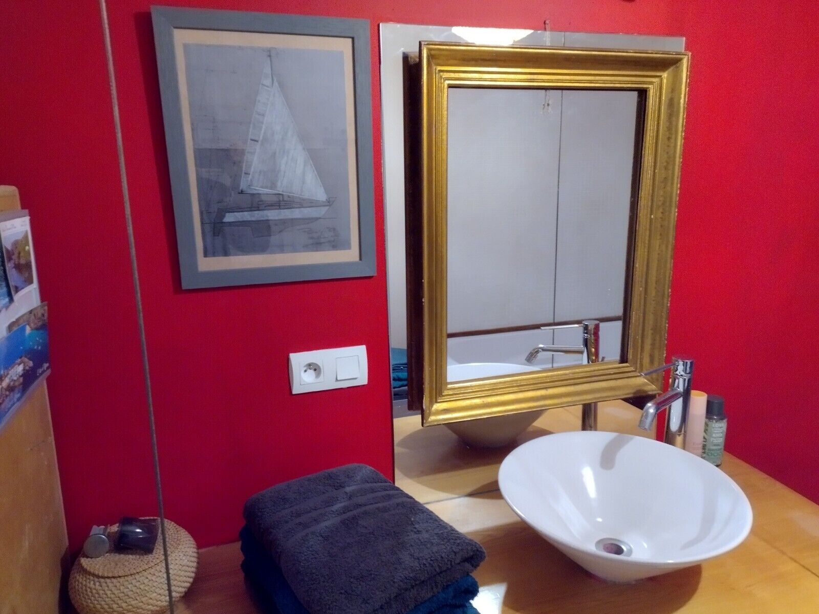 Een badkamer met een rode wand, een lijst met een afbeelding, een wastafel en een handdoek.