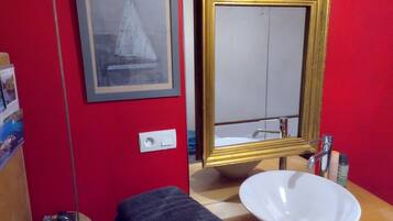 Een badkamer met een rode wand, een lijst met een afbeelding, een wastafel en een handdoek.