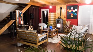 Een gezellige woonkamer met een houten trap, een open haard, een bank, een salontafel en een gitaar.