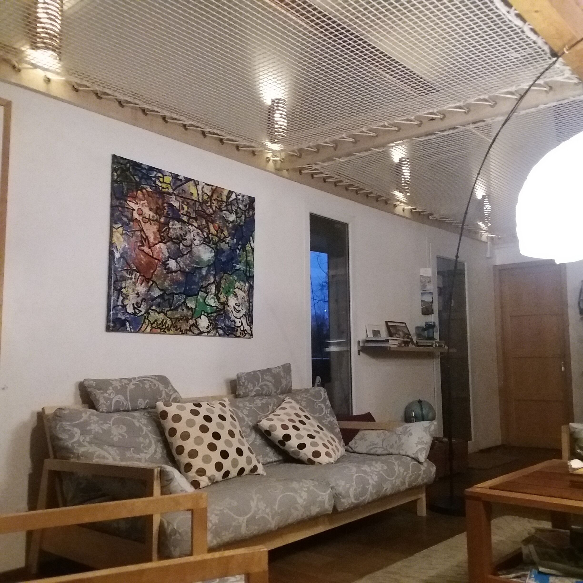 Un salon comprenant un canapé, un tableau abstrait aux couleurs vives, une table basse en bois et un plafond agrémenté d’un luminaire.