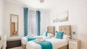 Een hotelkamer met twee bedden, een spiegel, een schilderij van de Eiffeltoren en een nachtkastje met een lamp.