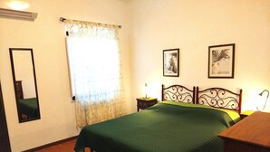 A bedroom with a bed, a nightstand, a mirror, a window with curtains, and two framed pictures on the wall. - Appartamento Olive La Burraia (GAMBASSI TERME)