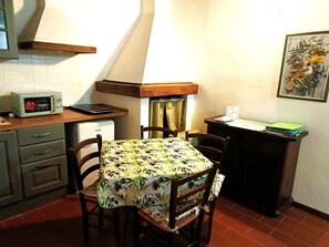 Une cuisine compacte équipée d’un four à micro-ondes, d’un petit réfrigérateur, d’une table recouverte d’une nappe à motifs floraux, de chaises en bois et d’un tableau accroché au mur.