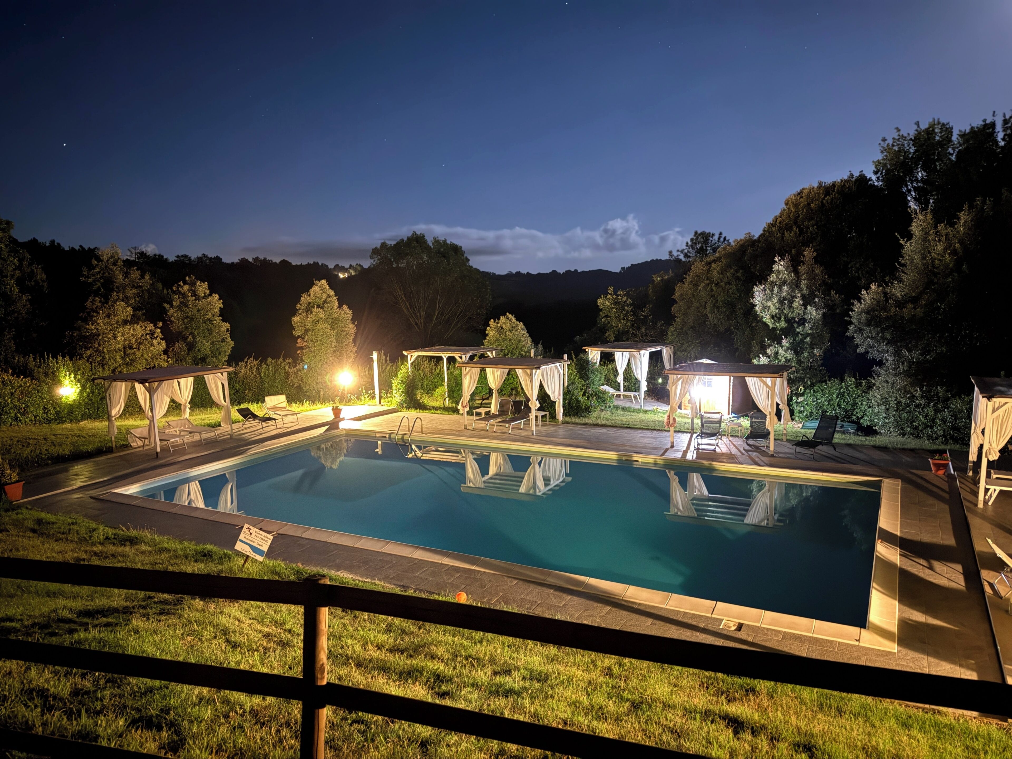 A rectangular swimming pool with a tiled deck, surrounded by lounge chairs and covered seating areas.